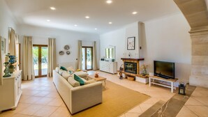 Un salón amplio con sofá, televisor, chimenea y vistas al exterior.