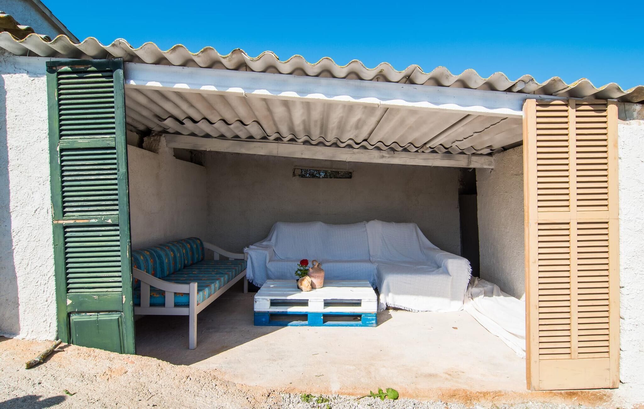 Un pequeño espacio al aire libre amurallado con un sofá blanco y una silla de madera con estampado azul y blanco, una mesa de centro de madera y una planta en maceta.
