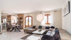 Ein modernes Wohnzimmer mit Sofagarnitur, einem Essbereich und einer durch eine offene Tür einsehbarer Küche.