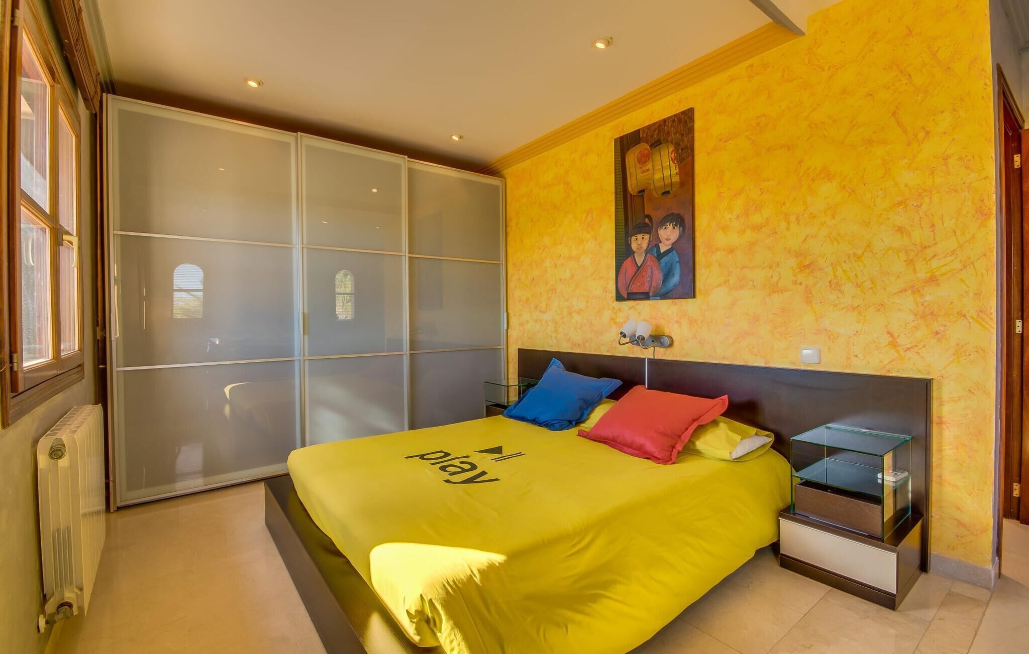 A bedroom with a bed, a nightstand, a glass cabinet, a sliding door closet, and a painting on the wall.