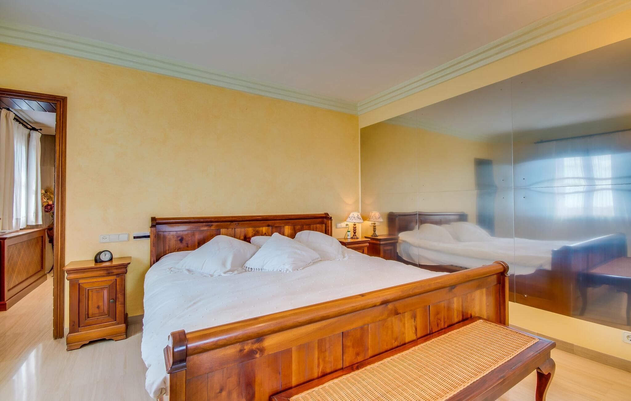 Una camera d'albergo con un letto in legno, comodini, uno specchio e un'ampia finestra.
