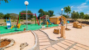 A playground with swings, slides, and a small wooden building. - Cozy home in Sant Llorenc with private swimming pool, can be inside or outside (Sant Llorenc)