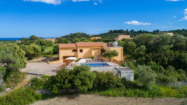 Eine mediterrane Villa mit Swimmingpool, umgeben von üppiger Vegetation und mit Blick auf eine Küstenlandschaft.