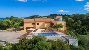 Eine Villa im mediterranen Stil mit Dachpool, Satellitenschüssel und Blick auf Meer und Hügel.