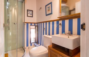 A bathroom with a glass shower enclosure, a toilet, and a sink with a wooden cabinet. - La Casa de los Espejos (Capdepera)