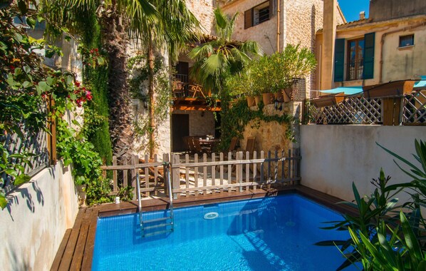 A swimming pool with a wooden deck, surrounded by lush greenery and stone buildings. - La Casa de los Espejos (Capdepera)