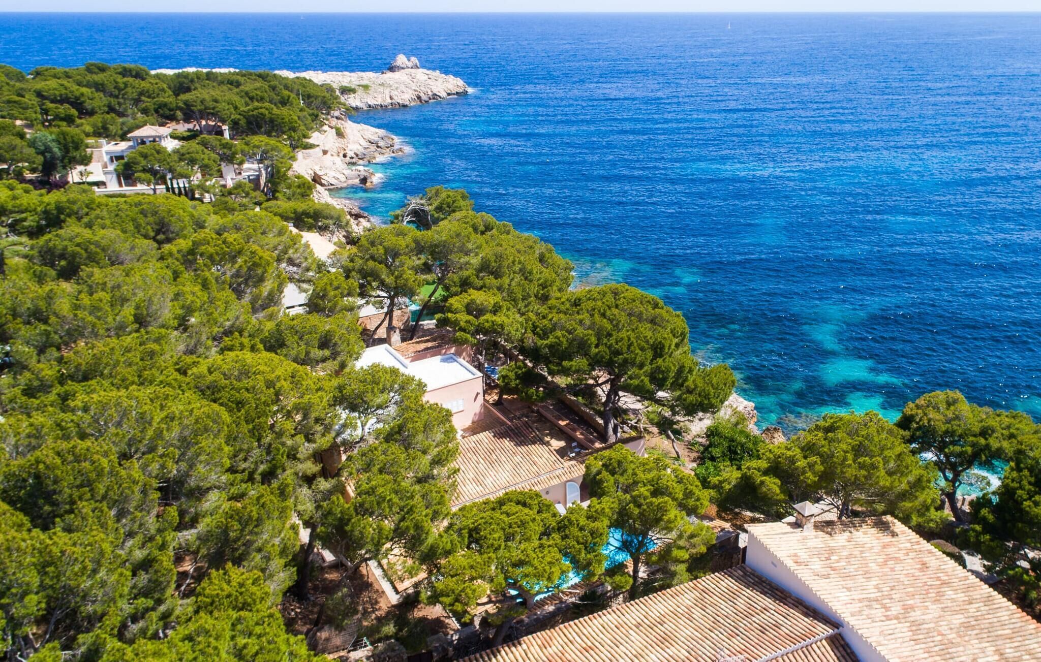 A coastal property with a view of the sea, surrounded by dense greenery and a rocky coastline.