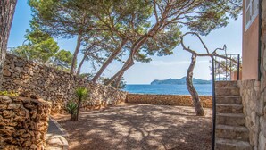A stone-walled courtyard with a gravel path leading to a staircase, overlooking a body of water and distant mountains. - Awesome home in Cala Ratjada (Cala Ratjada)