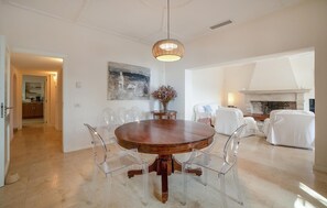 A dining area with a round wooden table, clear chairs, a hanging light fixture, and a fireplace in the background. - Awesome home in Cala Ratjada (Cala Ratjada)