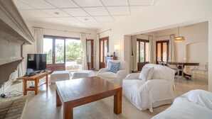 A spacious living room with a wooden coffee table, white sofas, a TV, and a dining area with a table and chairs. - Awesome home in Cala Ratjada (Cala Ratjada)
