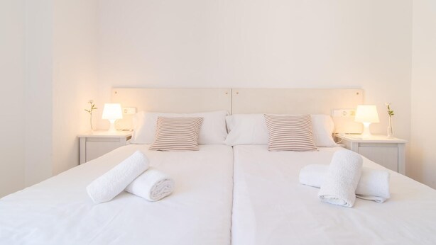 A double bed with white linens and striped pillows, two bedside tables with lamps, and rolled towels on the bed. - Awesome home in Arta with WiFi (Arta)