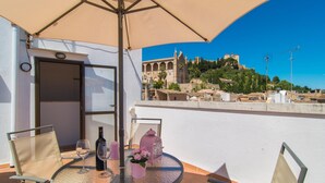 A balcony with a table, chairs, and a large umbrella. A bottle and glasses are on the table. A pink lantern and flowers are on the table. A building with a tower is in the background. - Awesome home in Arta with WiFi (Arta)