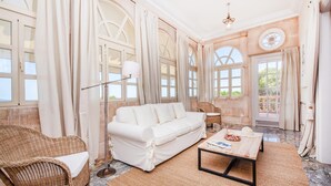 A spacious room with a white sofa, wicker chairs, a coffee table, and large windows with curtains. - La Casa de las Vistas (Palma)