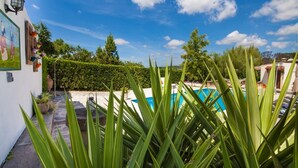 Un área de piscina bajo un cielo azul despejado, rodeada de abundante vegetación y un seto bien cuidado.