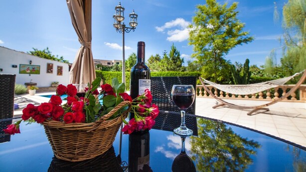 Una mesa con una botella de vino, una copa de vino y una cesta de rosas rojas.