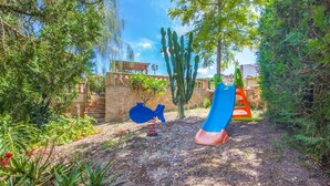 Un parque infantil con un tobogán y columpios, rodeado de cactus y otra vegetación.