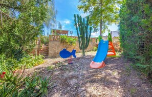 Ein Spielplatz mit Rutsche und Schaukeln, umgeben von Kakteen und anderer Vegetation.