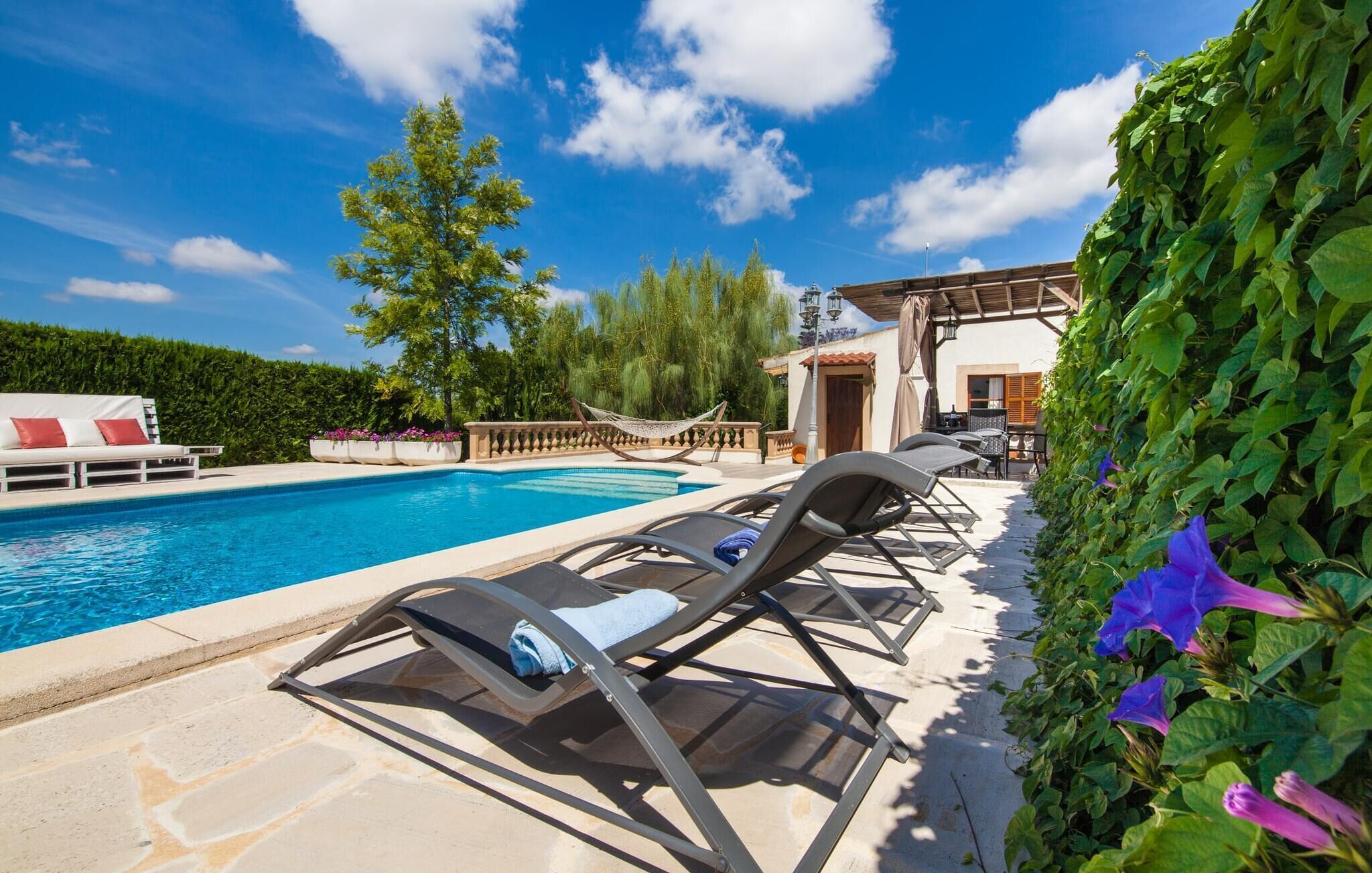 A poolside area with lounge chairs, a white sofa, and a building with a tiled roof.