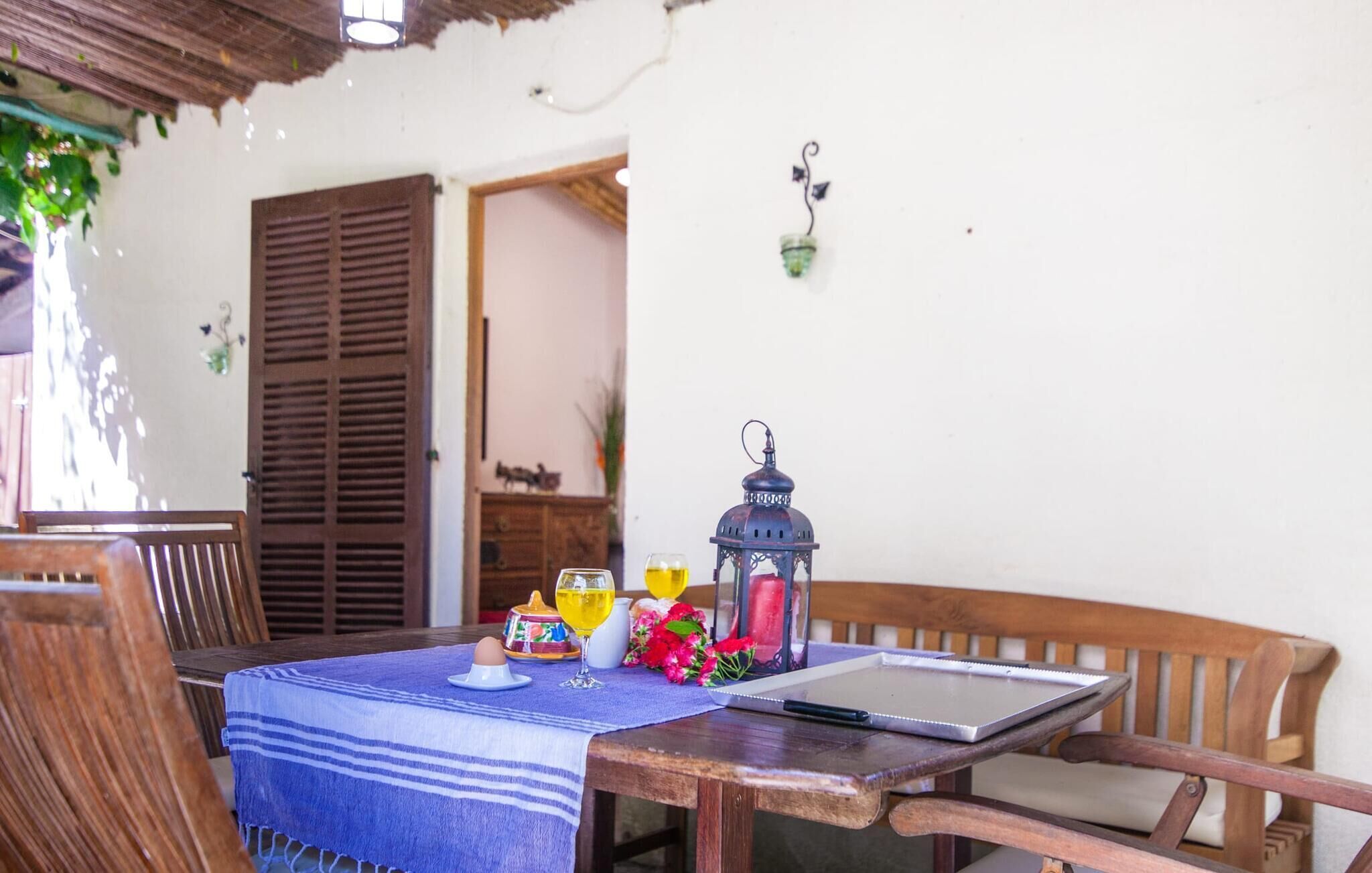 A wooden table with a blue tablecloth, a laptop, a glass of wine, a lantern, and a notebook.