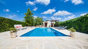Una piscina con sillas de descanso y una pérgola, rodeada de vegetación y un cielo despejado.