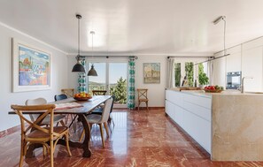 A dining area with a wooden table and chairs, a view of the outdoors, and a kitchen with a modern design. - Nice home in Pollenca with private swimming pool, can be inside or outside (Pollenca)