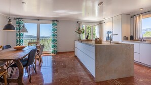 Una cocina moderna con una isla central, ventanas amplias y un comedor con mesa y sillas de madera.