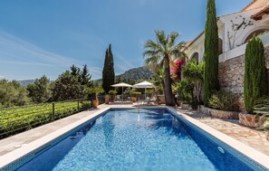 A swimming pool with a tiled edge, surrounded by potted plants, outdoor furniture, and a stone wall. - Nice home in Pollenca with private swimming pool, can be inside or outside (Pollenca)