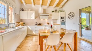 A modern kitchen with white cabinetry, a wooden dining table, and two white chairs. - Stunning home in Alcudia with private swimming pool, can be inside or outside (Alcudia)
