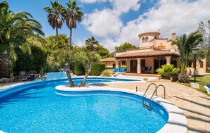 Ein Schwimmbecken mit einer Steindeckplatte, umgeben von Palmen und einem Haus mit einem Ziegeldach.