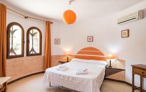 Ein Hotelzimmer mit einem Bett, zwei mit Vorhängen versehenen Fenstern, einer wandmontierten Klimaanlage und einer orangefarbenen Pendelleuchte.