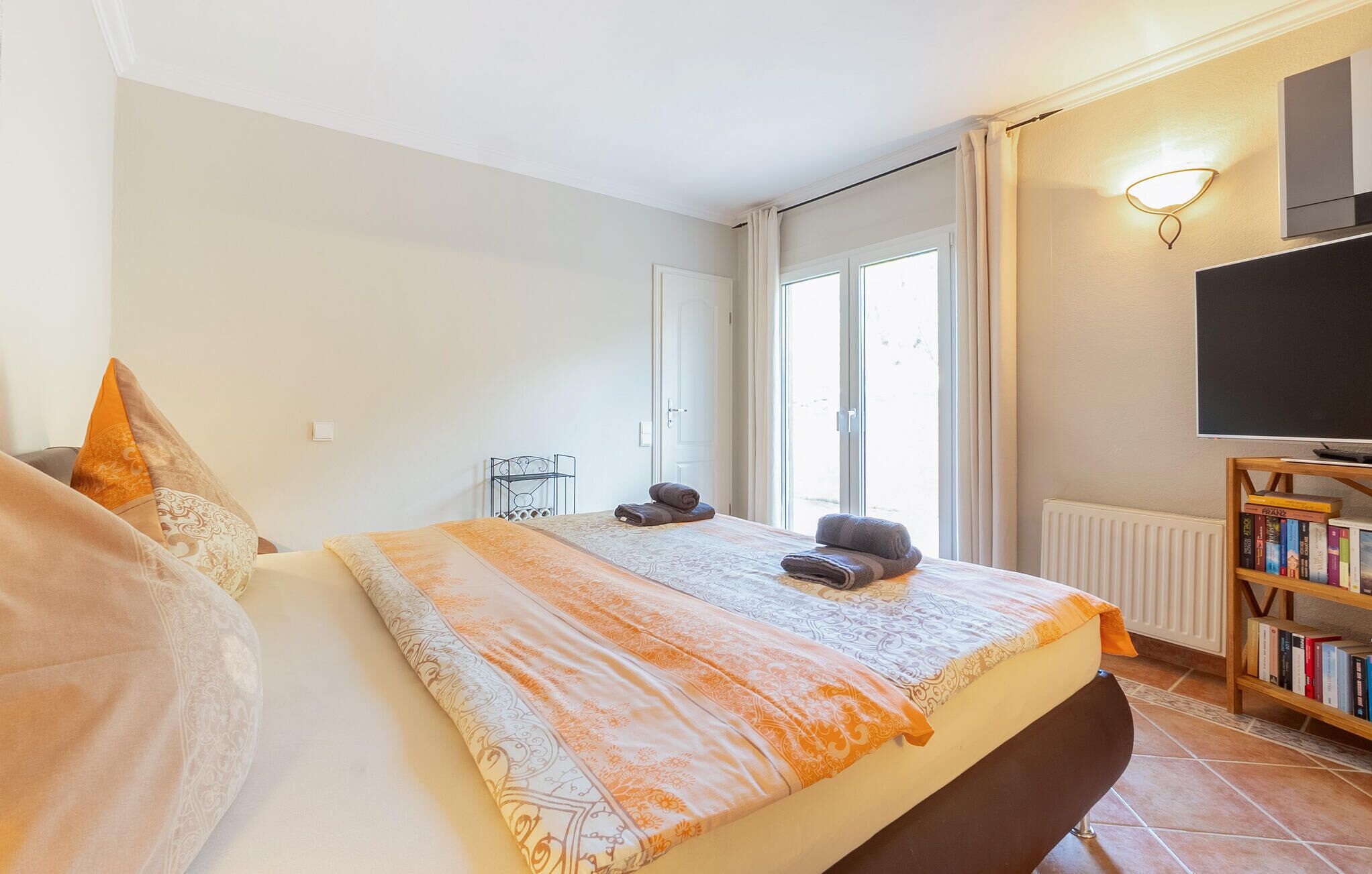 Ein Schlafzimmer mit Bett, Nachttisch, Bücherregal und Fenster.
