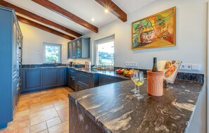 A modern kitchen with dark blue cabinets, a marble countertop, and a large window. - Beautiful home in Colonia de Sant Pere (Colonia de Sant Pere)