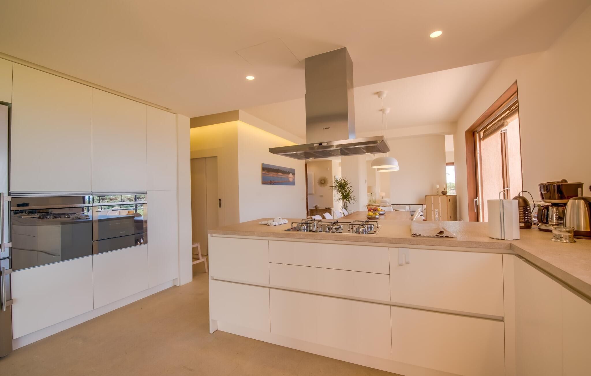 Een moderne keuken met een centraal eiland, roestvrijstalen apparatuur en een groot raam dat voor natuurlijk licht zorgt.