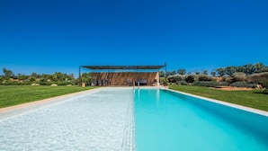 Una piscina rectangular de agua cristalina y azul, rodeada por un césped cuidado y un porche de madera con asientos.