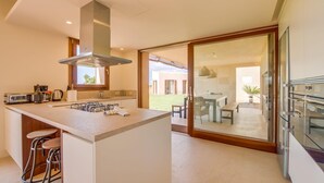 Una cocina moderna con una isla central, taburetes de bar, horno empotrado y un ventanal grande.