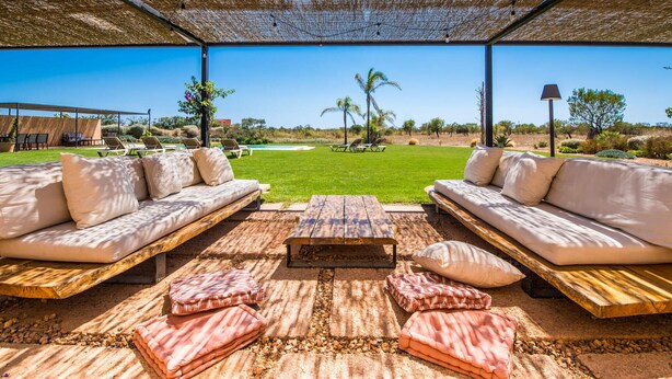 Un área de estar al aire libre con dos sofás y una mesa de madera, con vistas a un césped cuidado y palmeras.
