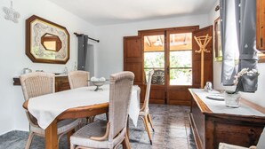 Ein Essbereich mit Holztisch, Korbstühle, einem dekorativen Spiegel und einem Fenster mit Holzjalousien.