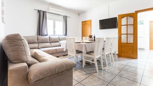 Ein Wohnzimmer mit einem beigen Sofa, einem Esstisch für vier Personen und einem an der Wand montierten Fernseher.