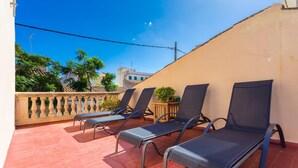 Eine Dachterrasse mit vier Liegestühlen, einem kleinen Tisch mit einem Blumentopf und einem Geländer.