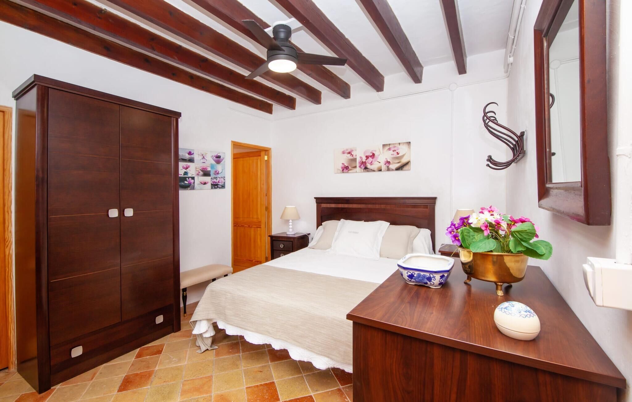 Une chambre avec une grande armoire en bois, un lit avec une tête de lit en bois, une table de chevet avec une lampe et une plante décorative.