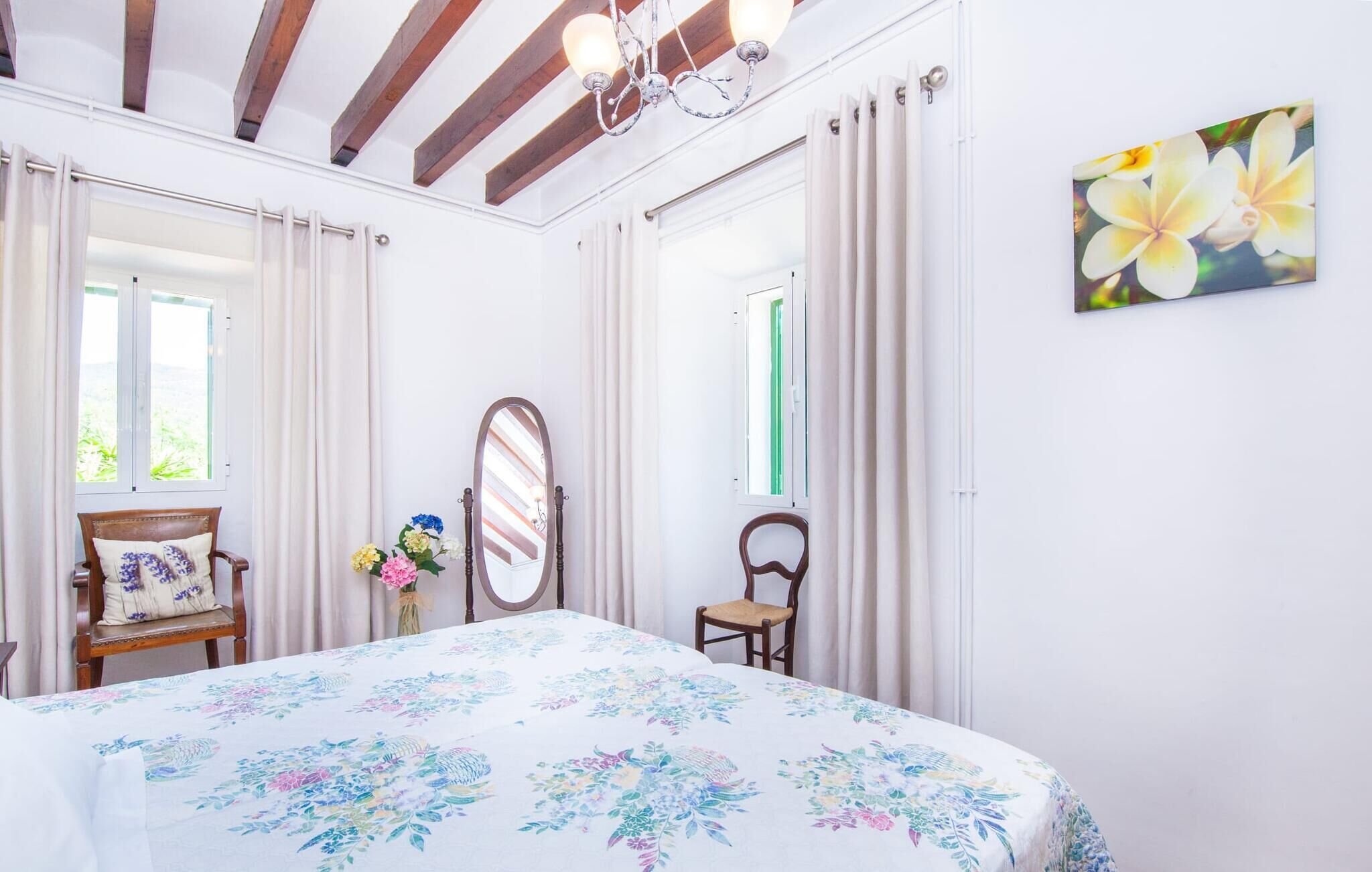 A bedroom with a bed, a chair, a mirror, and a window with curtains.