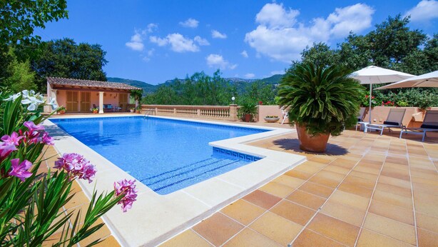 Una piscina con bordo piastrellato, un'area relax con sedie e ombrelloni, e vista sul paesaggio circostante.