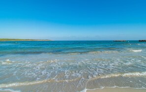 Ein Strand mit klarem, blauem Wasser, sanften Wellen und einer fernen Insel.