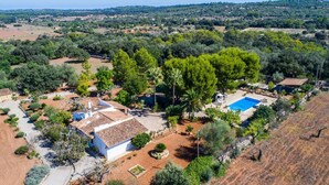 Vue aérienne d’une propriété dotée d’une piscine, d’un bâtiment blanc avec un toit en tuiles et d’une végétation luxuriante environnante.