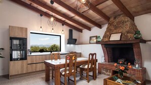 Une cuisine avec des poutres en bois, une cheminée en pierre et une vue sur l’extérieur.