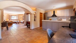 Un salón amplio con sofá, mesa de comedor y cocina con alacenas blancas y campana extractora negra.
