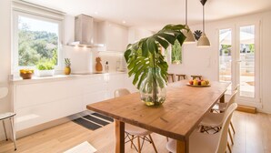 Eine moderne Küche mit weißen Schränken, einem Holztisch und einem großen Fenster mit Blick auf Grünflächen.