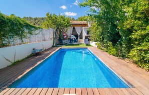 Une piscine rectangulaire dont le bord est recouvert de carrelage, entourée d’une terrasse en bois.