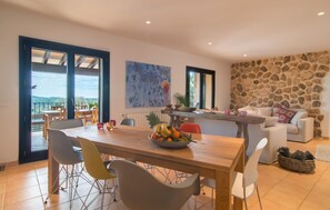 Een eetruimte met een houten tafel, kleurrijke stoelen en een fruitschaal. Er is een stenen muur en uitzicht op de omgeving.