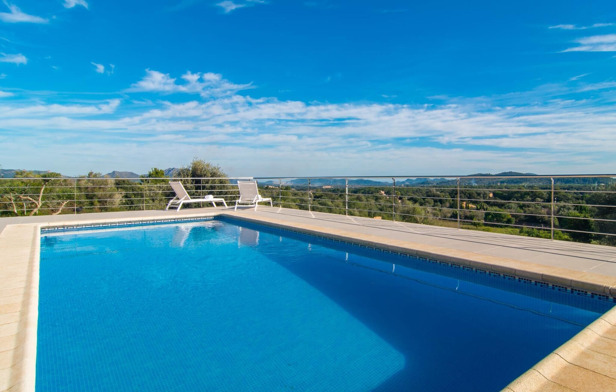 Piscina com duas espreguiçadeiras, cercada por guarda-corpo de metal, e vista para colinas distantes sob um céu limpo.